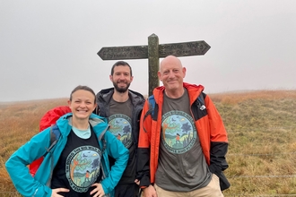 A woman and two men stood in front of a sign post on the Pennine way. The weather is misty.