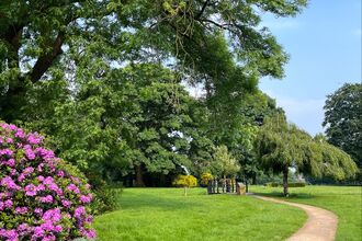 A path runsa through a park with trees and flowers on the left of the path. 