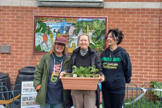 3 women standing outside Belgrave Community Library holidng a large planter