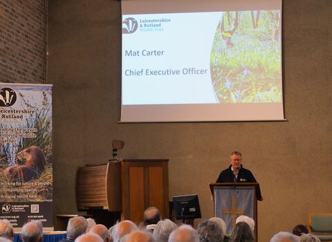 A man standing in front of a group of people. A presentation slide behind him says Mat Carter, Chief Executive Officer